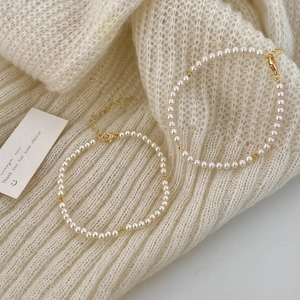 Elegant pearl necklace and bracelet set with gold clasp on white knit sweater
