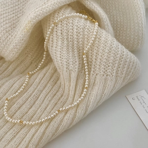 Close-up of elegant pearl necklace with gold beads on a soft knit sweater background