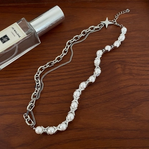 Detail of star-patterned pearls and chunky silver chain necklace on wood surface