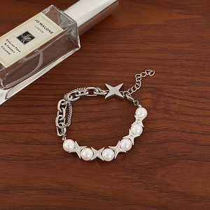 Detail of silver chain bracelet with faux pearls and four-pointed stars on wood surface