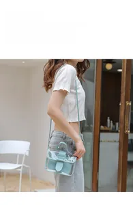 Detail of light blue transparent PVC crossbody bag with buckle and top handle held by model