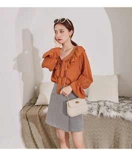 Detail of a beige quilted chain bag paired with an orange ruffle blouse and grey skirt