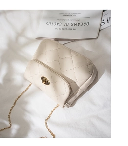 Detailed macro of cream quilted crossbody bag with gold chain and twist lock on a textured cloth