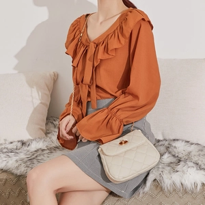 Beige quilted chain cloud bag with gold twist lock and orange ruffled blouse ensemble