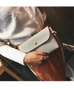 Detail of light grey pebbled leather crossbody bag featuring a gold spherical clasp