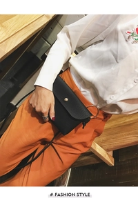 Detail of black pebbled leather crossbody bag with golden round buckle worn by model