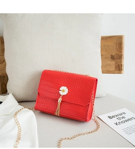 Dettaglio borsa rossa con trama a coccodrillo, charm margherita e catena dorata