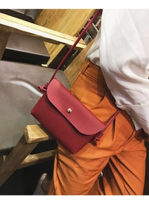 Detail of red lychee pattern leather crossbody bag with decorative gold metal buckle