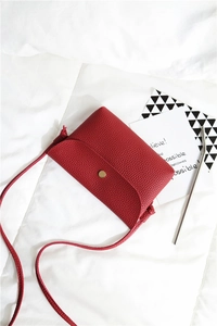 Detail view of red lychee textured small crossbody bag with a round golden magnetic buckle