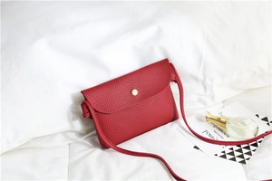 Detail of red crossbody bag with lychee texture and golden snap button on white bedding