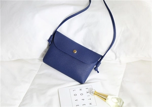 Detail of blue pebble-leather crossbody bag with gold buckle on white bedding