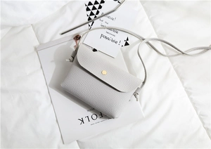 Detail of minimalist cream PU leather crossbody bag with golden round buckle and litchi texture