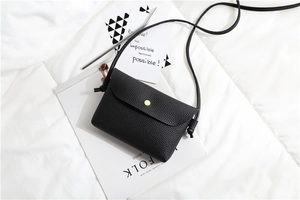 Detail of black pebbled leather crossbody bag with golden button on a white background