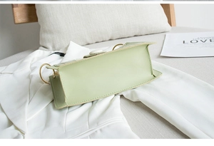 Dettaglio borsa a mano verde chiaro con texture litchi e hardware dorato su giacca