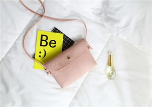 Detail of light pink pebble leather crossbody bag featuring a gold round metal buckle