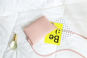 Detail of light pink pebble grain leather crossbody bag next to a perfume bottle