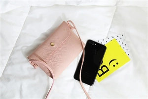 Detail of pink mini crossbody bag with lychee texture and gold button on white bedding