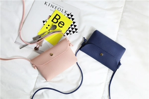 Detail view of pink and navy blue pebble leather crossbody bags on a white textured fabric