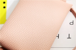 Macro shot of light pink litchi grain leather texture on elegant crossbody bag