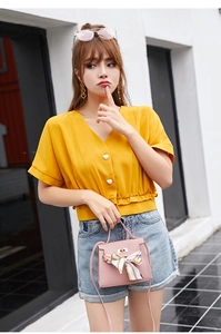 Close-up of ginger yellow V-neck top featuring white heart buttons and ruffled hem detailing