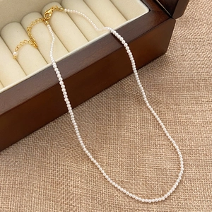 Close-up of a delicate white pearl necklace with golden lobster clasp and extender