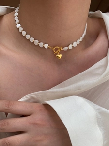 Detail of a gold heart necklace with white mother of pearl beads and a stylish OT clasp