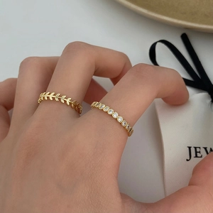 Close-up of a gold-plated leaf ring and a zircon paved band set on a display plate