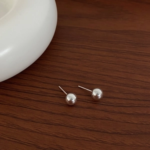 Polished silver sphere stud earrings displayed on a dark wooden surface with white ceramic
