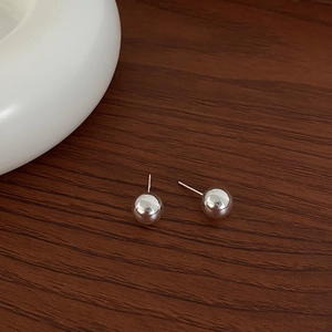 Close-up of polished silver ball stud earrings on a natural wood surface with ceramic