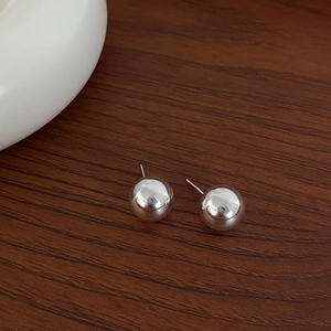 Detailed close-up of minimalist silver ball stud earrings on a dark wood background