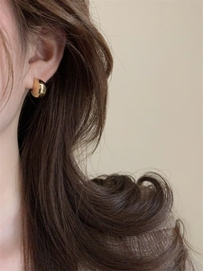 Detailed close-up of a model wearing a thick C-shaped gold hoop earring with a mirror finish