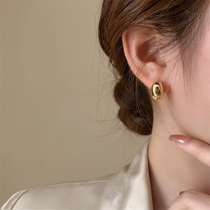 Close-up of elegant gold bean stud earrings with a polished mirror finish on model