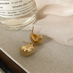 Close-up of golden bean earrings with mirror polish finish on white textured tray