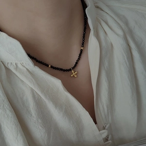 Elegant black beaded choker necklace with golden floral pendant on a white shirt background