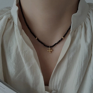 Close-up of elegant black beaded necklace with a gold cross pendant on a model
