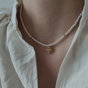 Detailed view of elegant pearl necklace featuring a golden minimalist cross pendant
