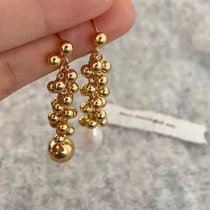Asymmetric long gold drop earrings featuring a metallic ball and a teardrop pearl pendant