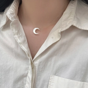Close-up of a crescent shell pendant on an invisible fishing line necklace on a model