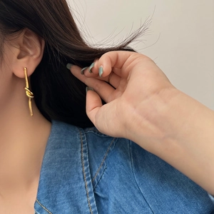 Dettaglio di orecchini pendenti a nodo dorati indossati da una modella in denim