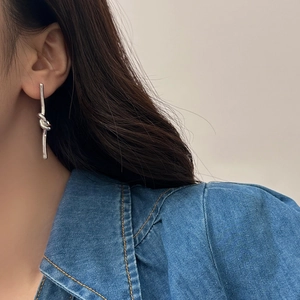 Dettaglio di un orecchino pendente in argento a nodo indossato da una modella