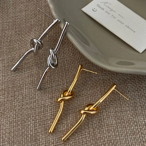 Dettaglio di orecchini a nodo minimalisti in oro e argento su tessuto morbido