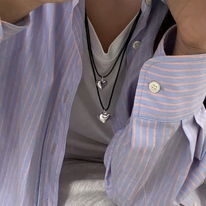 Detail of double heart pendants on black woven cord worn over a striped shirt