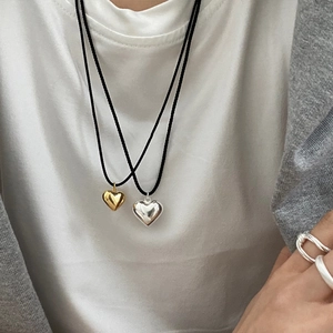 Close-up of gold and silver heart pendants on black cords with stylish silver rings