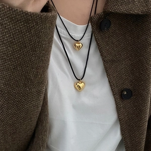Detail of layered gold heart pendants on black woven cord worn over a tweed jacket