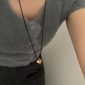 Detail of 3D gold heart pendant on a black cord necklace worn over blue knit cardigan