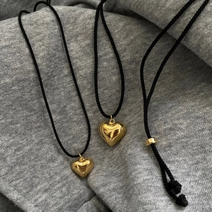 Close-up of golden heart pendant on black braided cord with adjustable metal slider