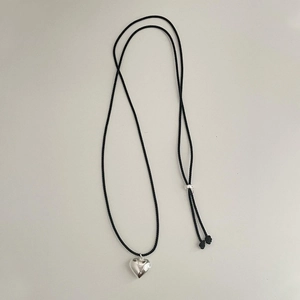 Close-up of polished silver heart pendant with black braided cord and adjustable silver knot