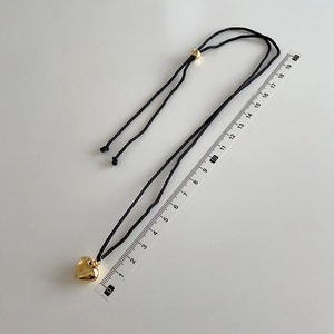 Macro shot of 3D gold heart pendant with black cord and adjustable gold beads