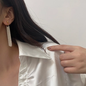 Close-up of long silver fringe tassel earrings with gold stud on a model in white silk