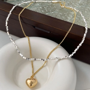 Close-up of double-layer necklace with heart pendant on white ceramic and wood tray